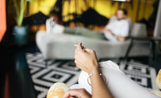 Cropped image of woman smoking while sitting against man on sofa at home