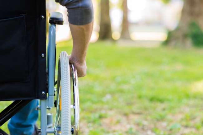 Male hand on wheel of wheelchair during walk in park