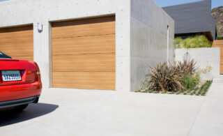 concrete driveway and garage with wooden garage door and partial view of red car parked nearby