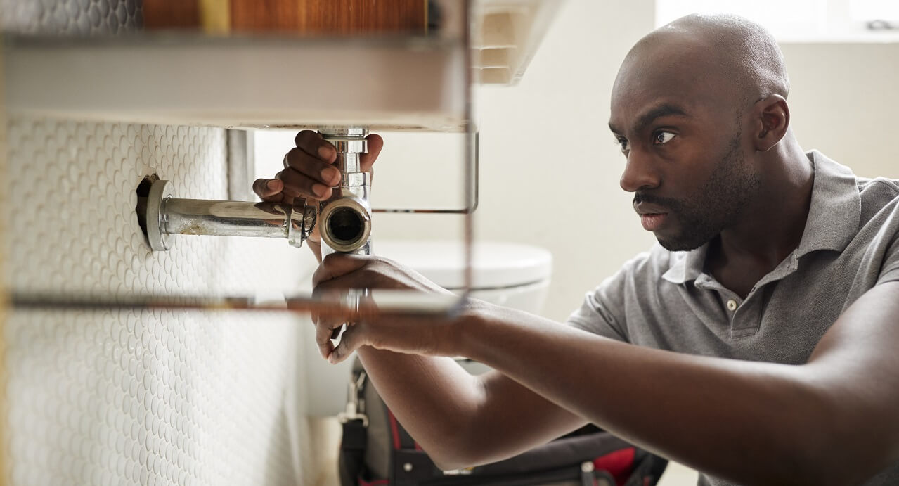 plumber from a plumbing company under sink installing pipes