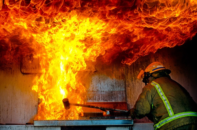 Firefighter putting out a large kitchen fire coming from stove