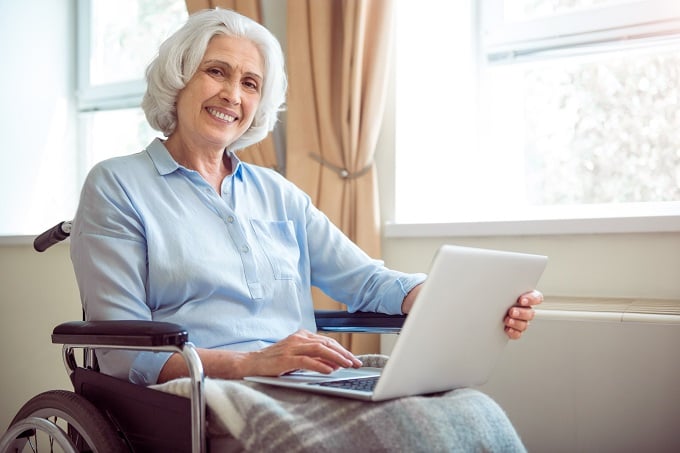 Digitalization. Cheerful and positive senior woman in wheelchair using laptop