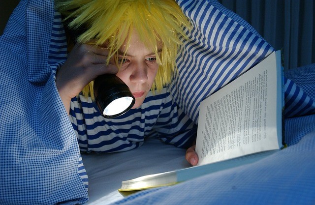 kid reads book under covers in bed