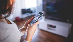 A woman in a grey shirt turns on the television with her smart phone.