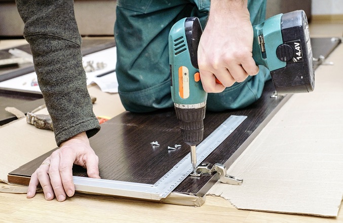 Assembling furniture from chipboard, using a cordless screwdriver, close up.