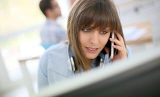 Young woman talking on smartphone in front of desktop