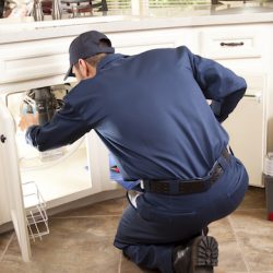 HVAC maintenance man works under the sink near the dishwasher.