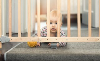 child playing behind safety gates in front of stairs at home