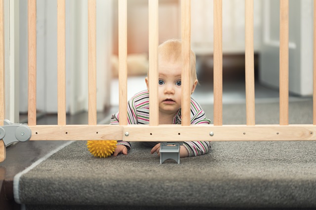 child playing behind safety gates in front of stairs at home