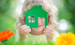 Happy child holding green house in hands with green background.