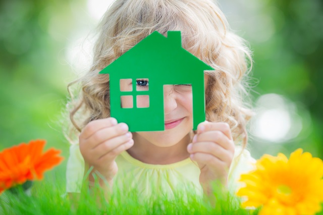 Happy child holding green house in hands with green background.