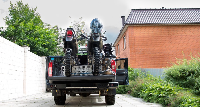 Rear view with two dirt bike motorcycles on the back of the camo truck with safety gear in residential setting.