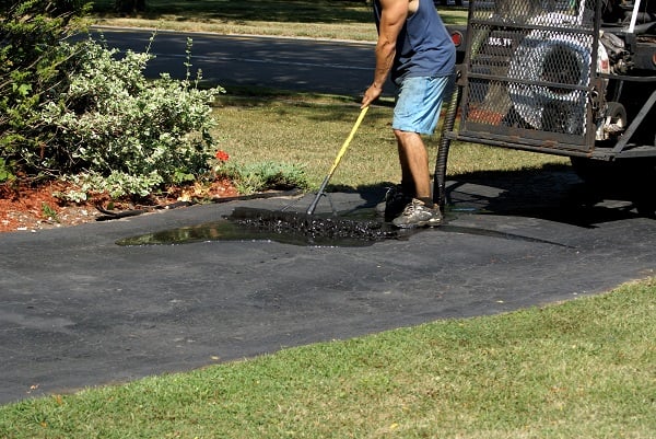 man adds sealer to his asphalt driveway