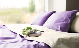 Lilac color accent in modern interior. Comfortable bed with book and bouquet in bedroom