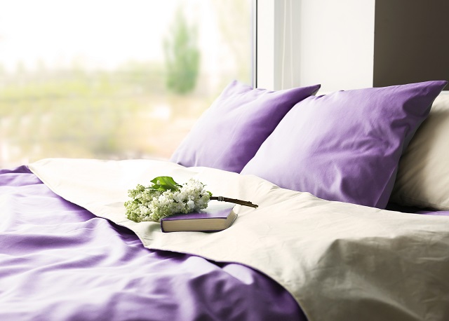 Lilac color accent in modern interior. Comfortable bed with book and bouquet in bedroom