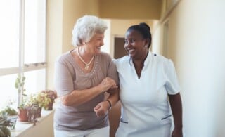 Smiling home caregiver and senior woman walking together