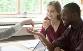 Real estate agent handing house keys to young happy couple