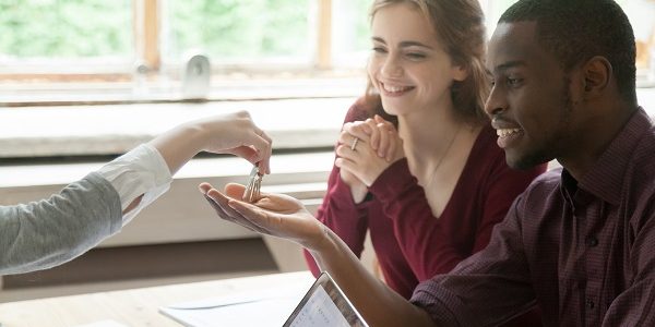 Real estate agent handing house keys to young happy couple