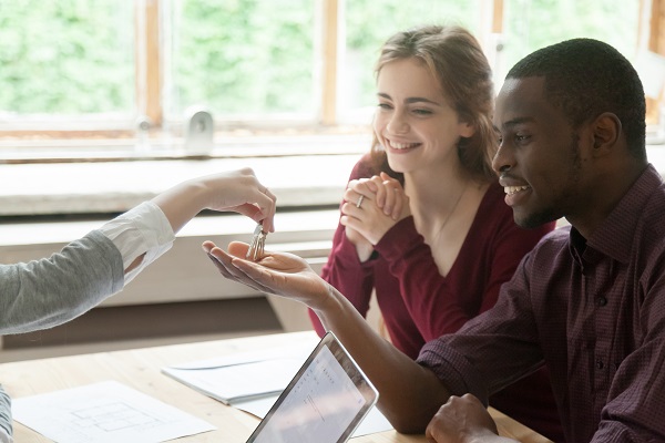 Real estate agent handing house keys to young happy couple