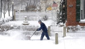 man uses a snow blower to remove snow from sidewalk