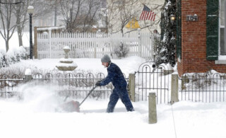 man uses a snow blower to remove snow from sidewalk