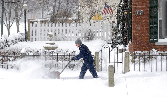 man uses a snow blower to remove snow from sidewalk