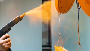 Powder coating of metal parts. A man in a protective suit sprays powder paint from a gun on metal products.
