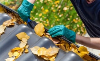 Man with gloved hands cleaning out leaves from a gutter
