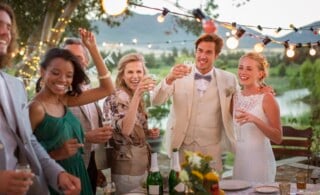 Young couple and guests toasting with champagne during wedding reception in backyard