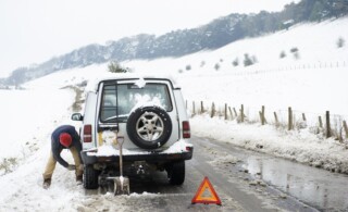 Man working on broken down car in snow