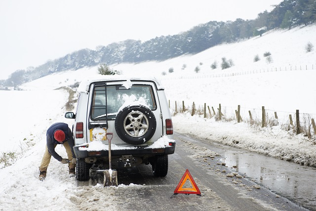 Man working on broken down car in snow