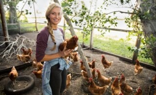 Smiling young female farmer holding chicken in chicken coop