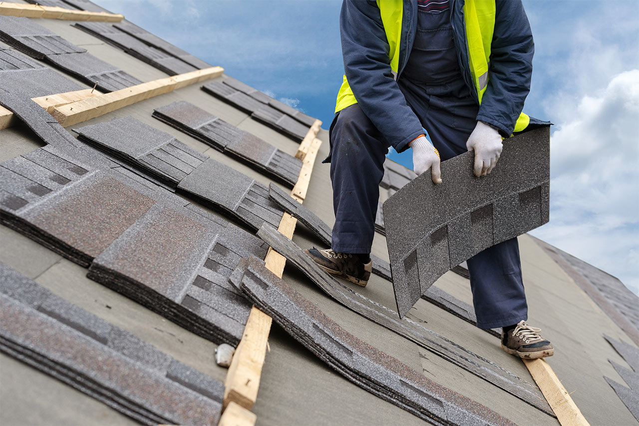 Construction workers install shingles at the top of the house