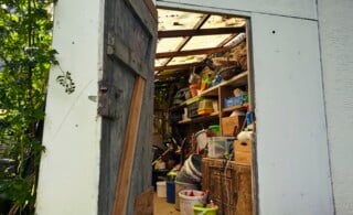 Interior of a garden shed with a crammed collection of eclectic diy and gardening equipment viewed through the open shed door.