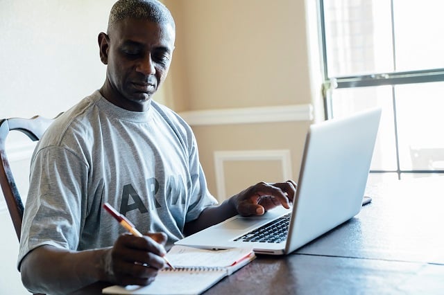 Middle aged man in army shirt working on laptop at home