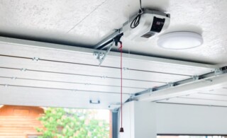 Opening door and automatic garage door opener electric engine gear mounted on ceiling with emergency cord. Double place empty garage interior with rolling entrance gate.