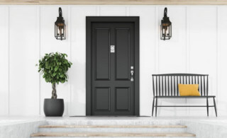 dark front door against white house next to tree, sconces and a metal bench