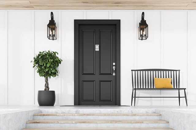 dark front door against white house next to tree, sconces and a metal bench