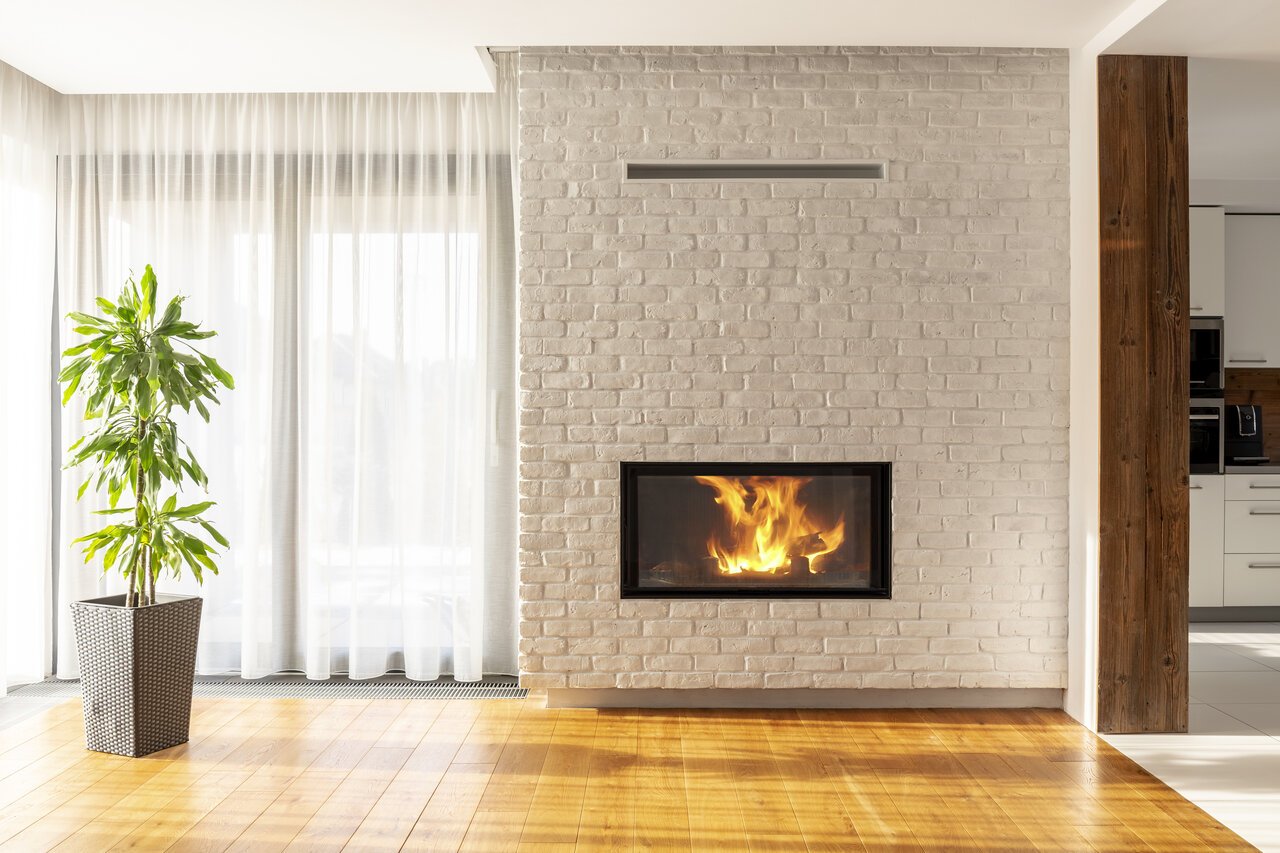 Fireplace on brick wall in bright living room interior of house with plant and windows