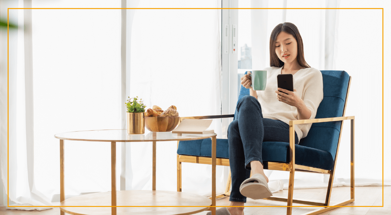 Woman sitting on chair looking at phone with coffee cup in other hand