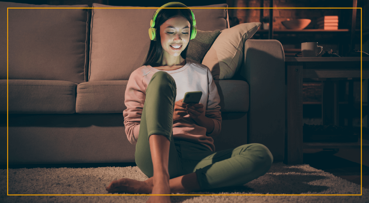 woman with headphones on sitting on the living room rug looking at phone