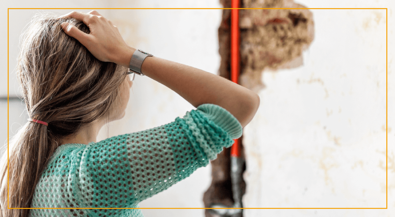 Woman with hand on head looking at broken pipe