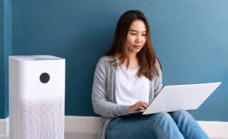 Young woman sitting near air purifier with laptop