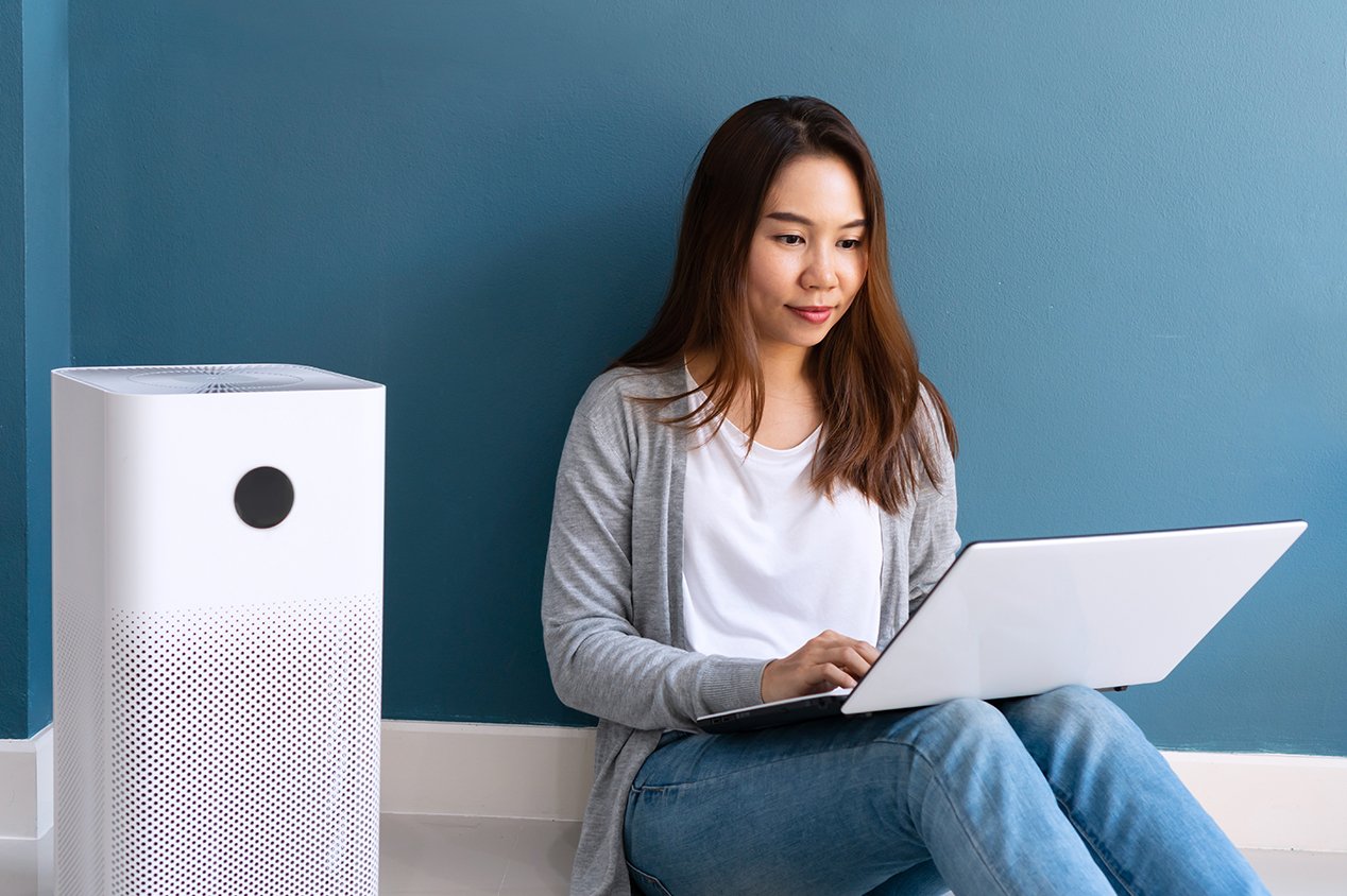 Young woman sitting near air purifier with laptop