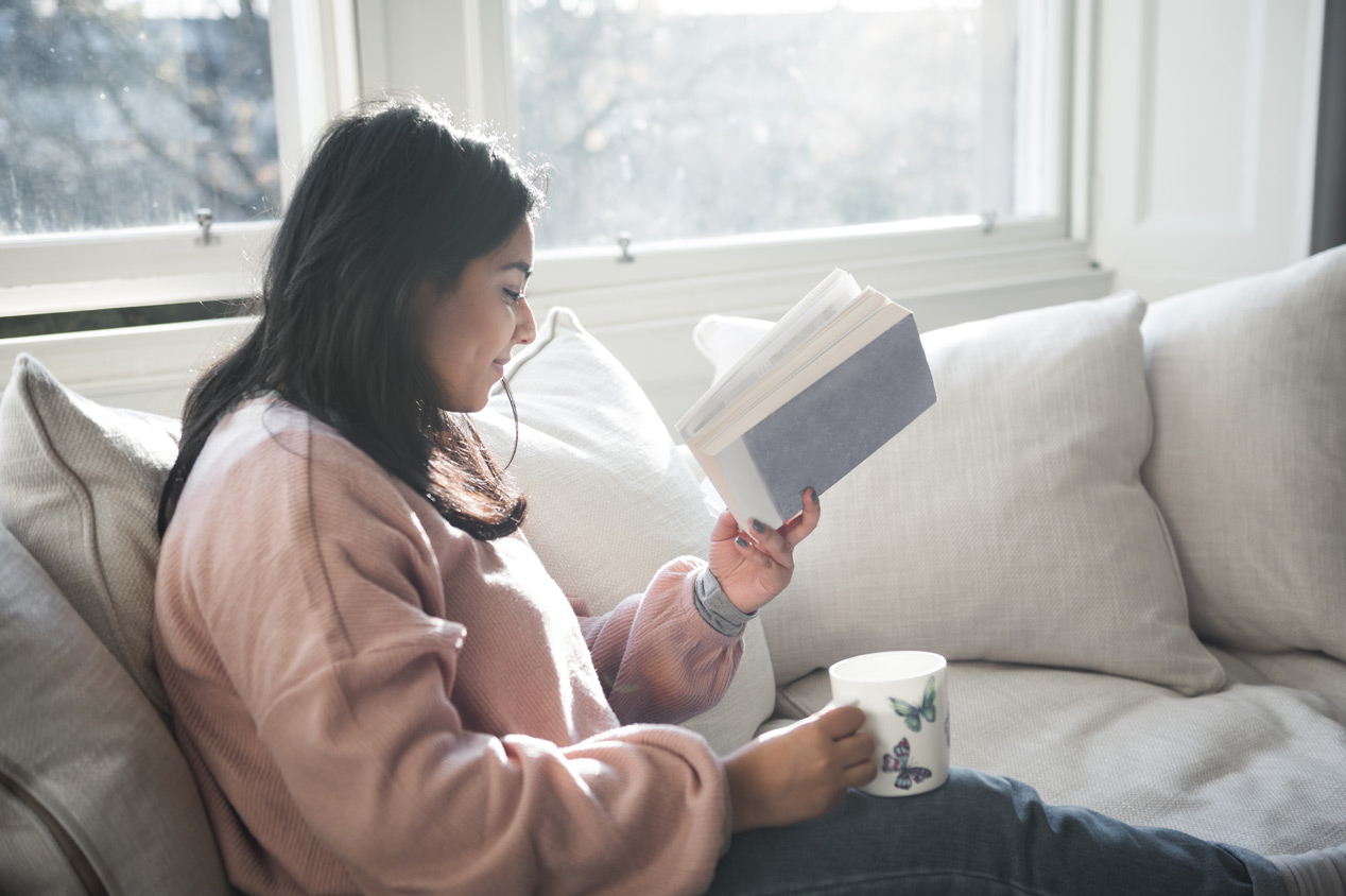 A woman drinking tea while reading by the window