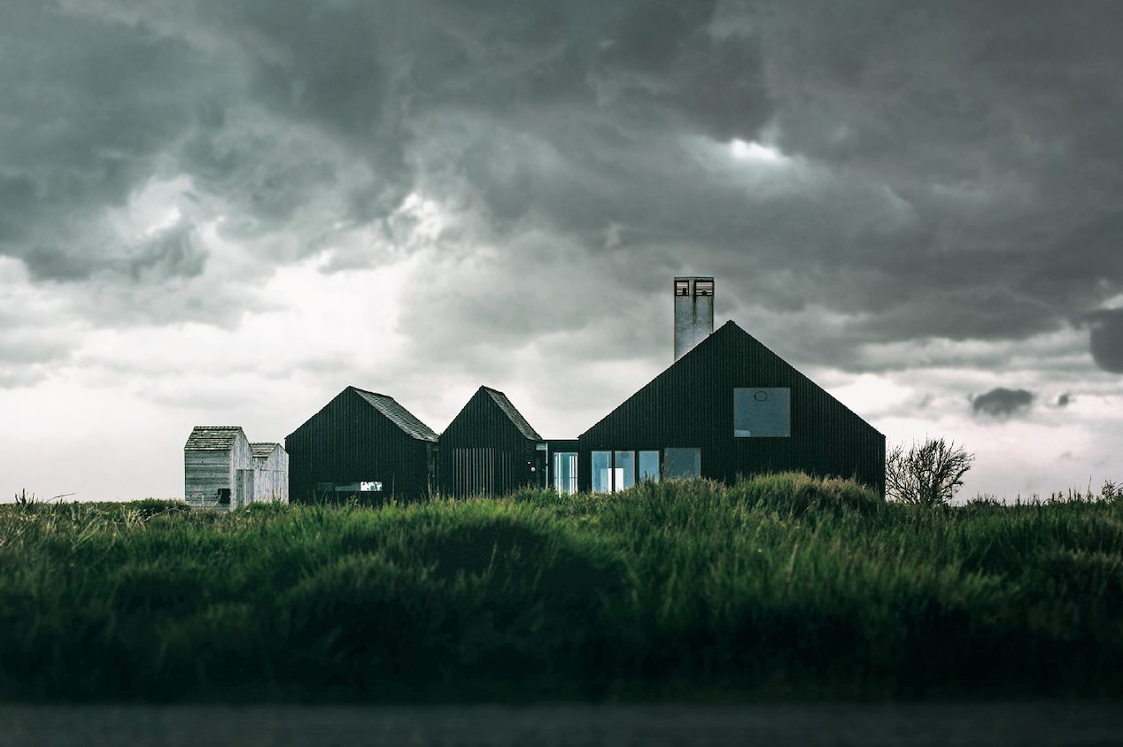 A large house across a grassy field with dark grey clouds casting shadows overhead