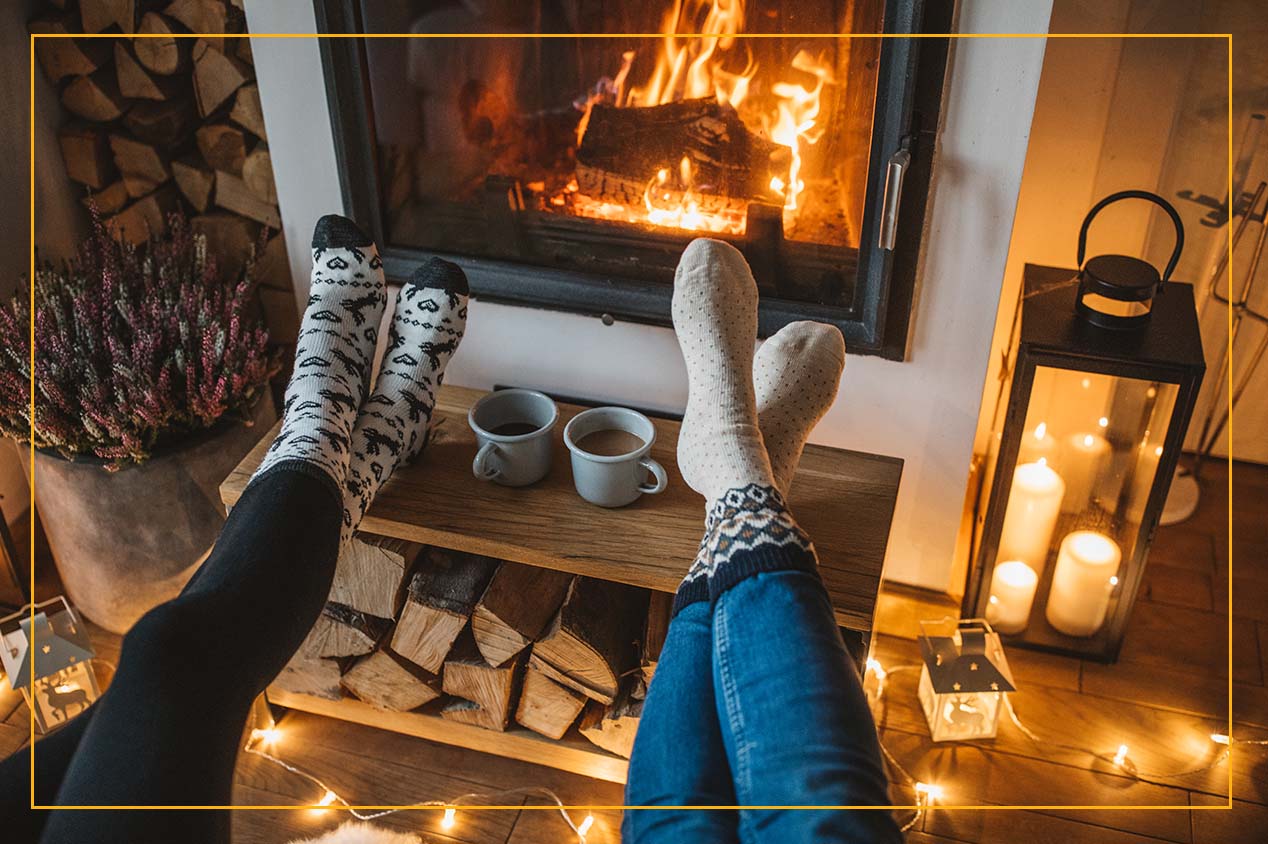 two people with socks on with their feet up on a coffee table by fireplace