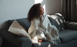 a woman wrapped in a blanket smiles on her couch